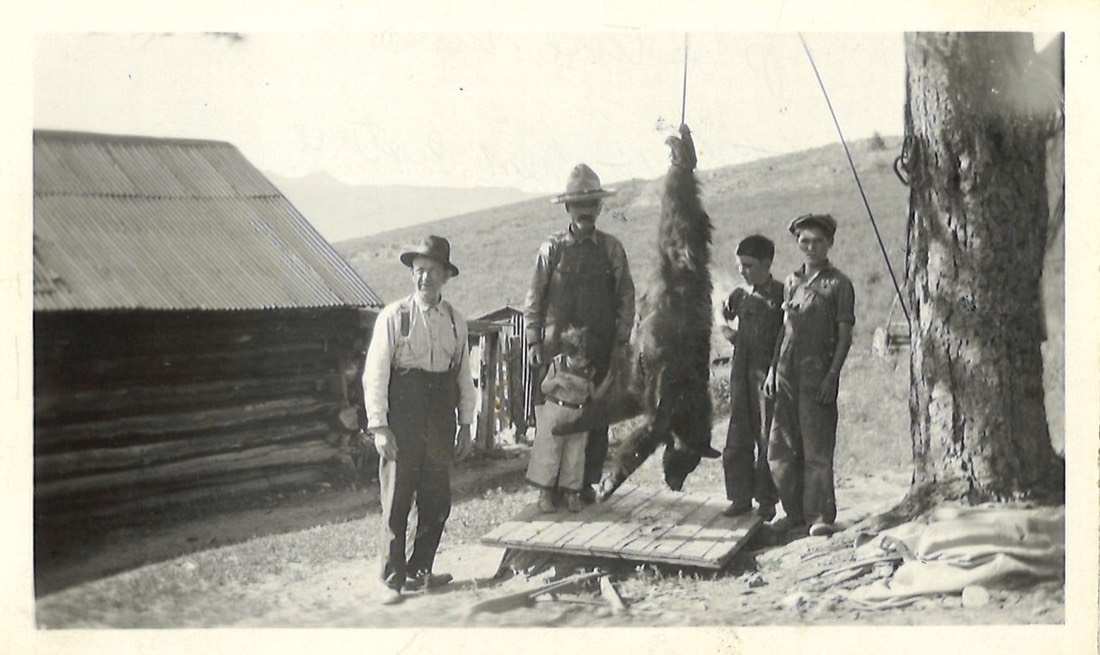 1931 photograph of the Pastore family beside a bear at the ranch, log cabin behind
