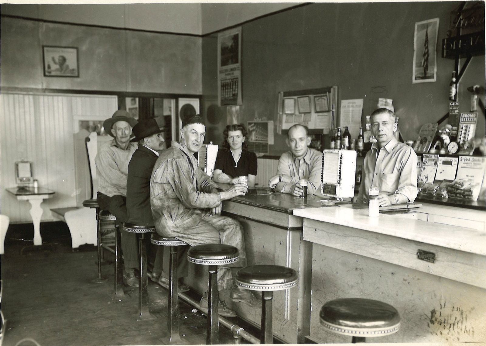 Six regulars at a mid-century Boulder bar, beer taps and punchboards on the counter
