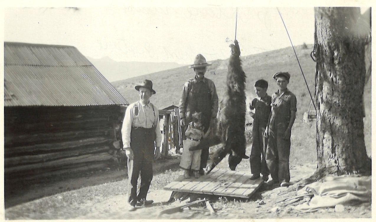 A bear hung from a pine beside the homestead cabin, the family gathered around
