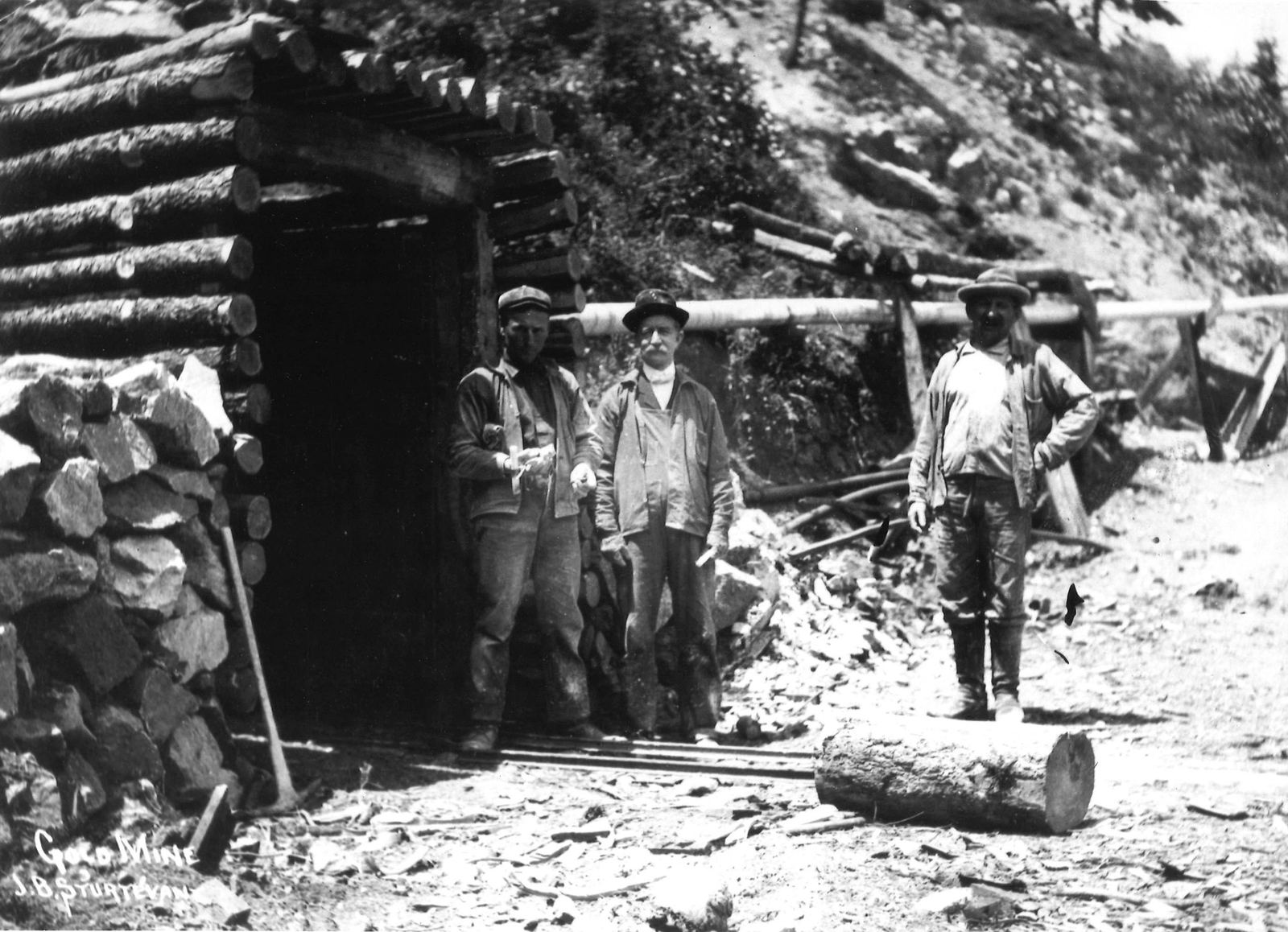 Three miners at a timbered gold mine portal, photographed by J. B. Sturtevant
