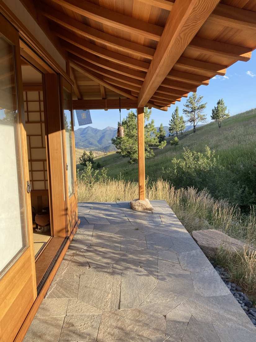 The teahouse porch: curved timber eave, shoji door, hanging bell, stone patio, mountains beyond