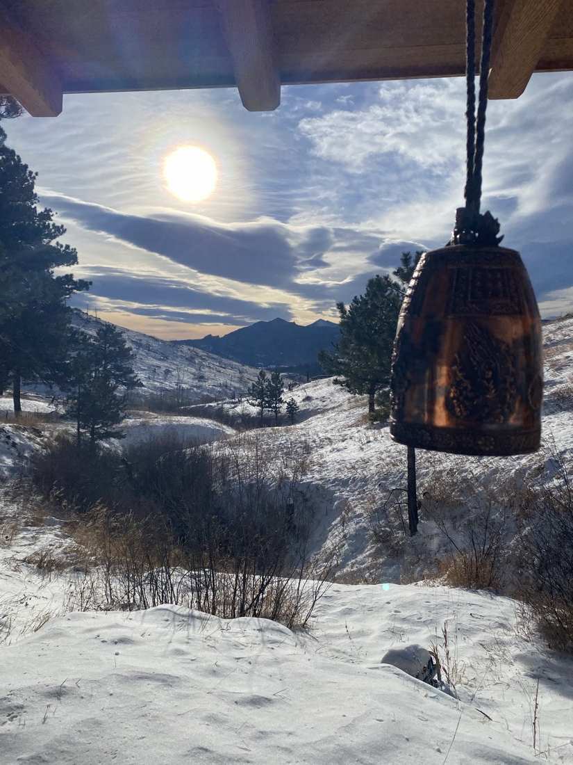 The bronze bell hanging from the eave against low winter sun and snowy peaks