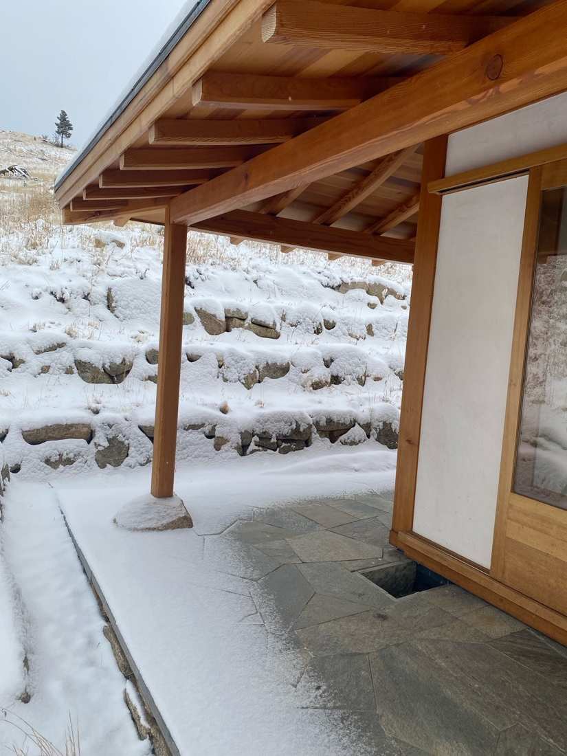 Timber rafters, shoji panel, flagstone patio, and snow-dusted stone wall